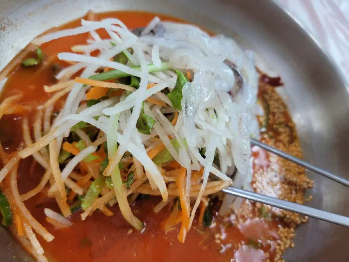 젓가락으로 집어 올린 물회 속 얇게 채 썬 무채와 당근