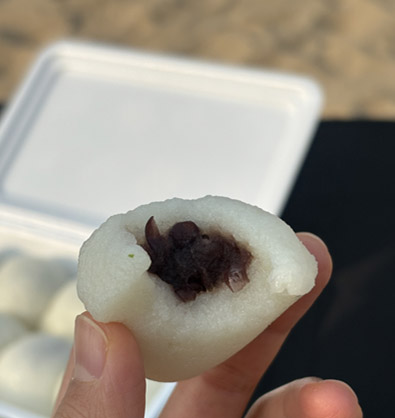 A bitten piece of Yukgu Bangatgan chapssal mochi showing the red bean filling and grainy rice cake skin