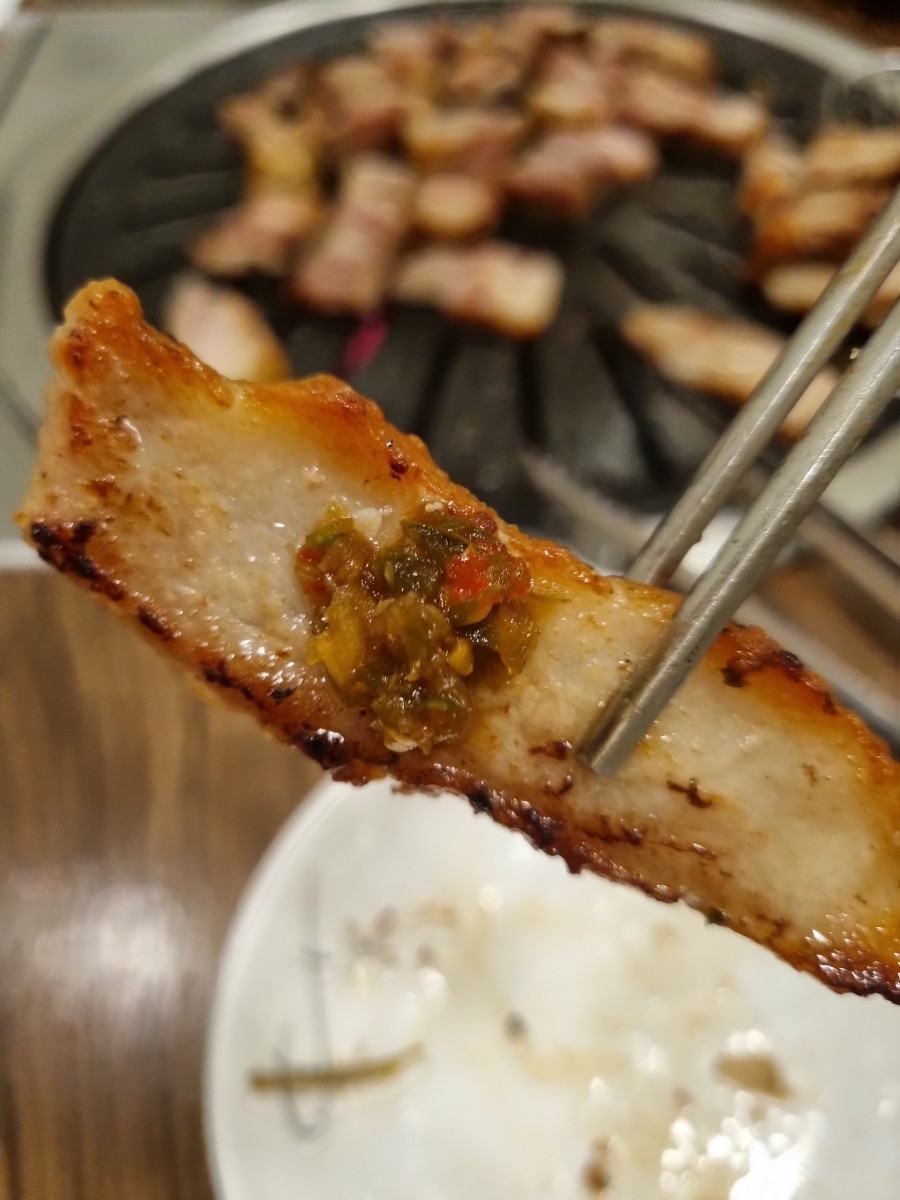 Grilled pork belly bite held by tongs