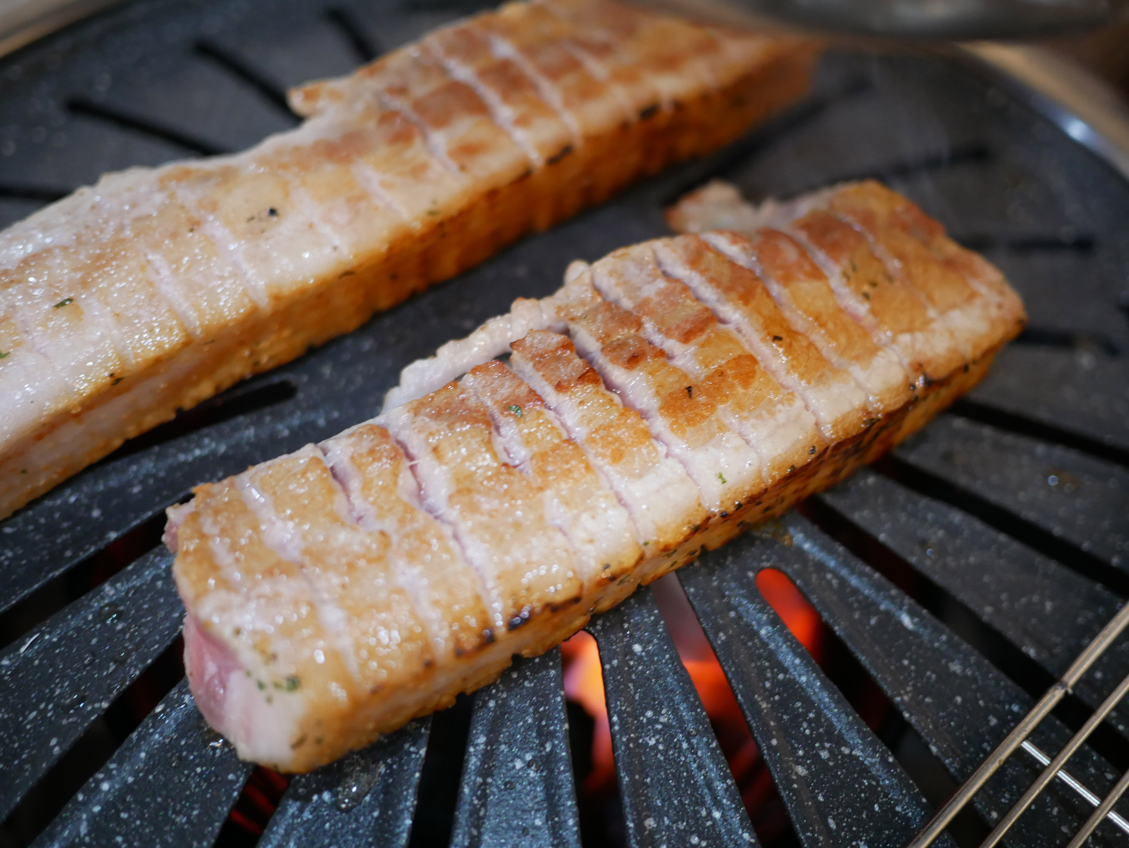 Thick pork belly grilling on a charcoal grill