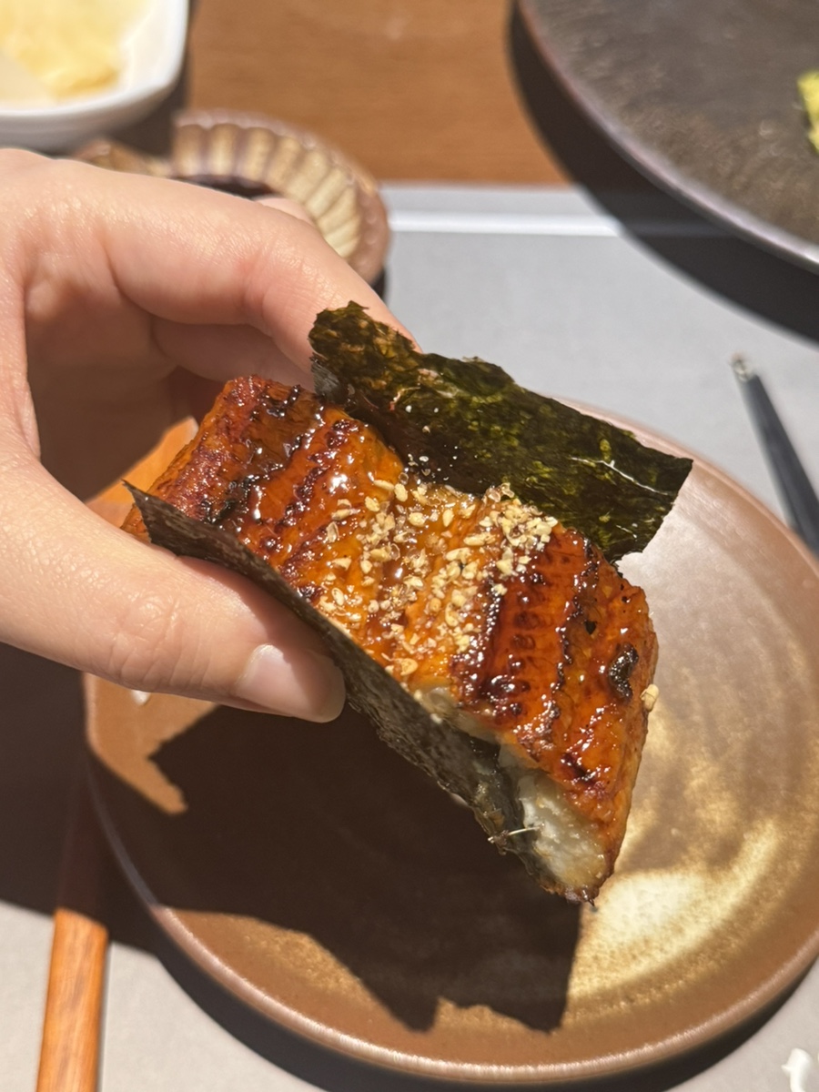 Hand holding a piece of grilled eel wrapped in seaweed