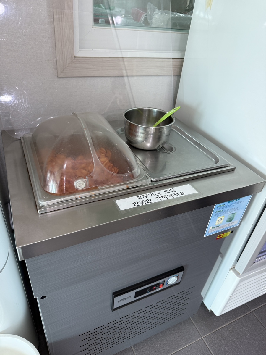 Self-serve stainless steel container of radish kimchi at the counter