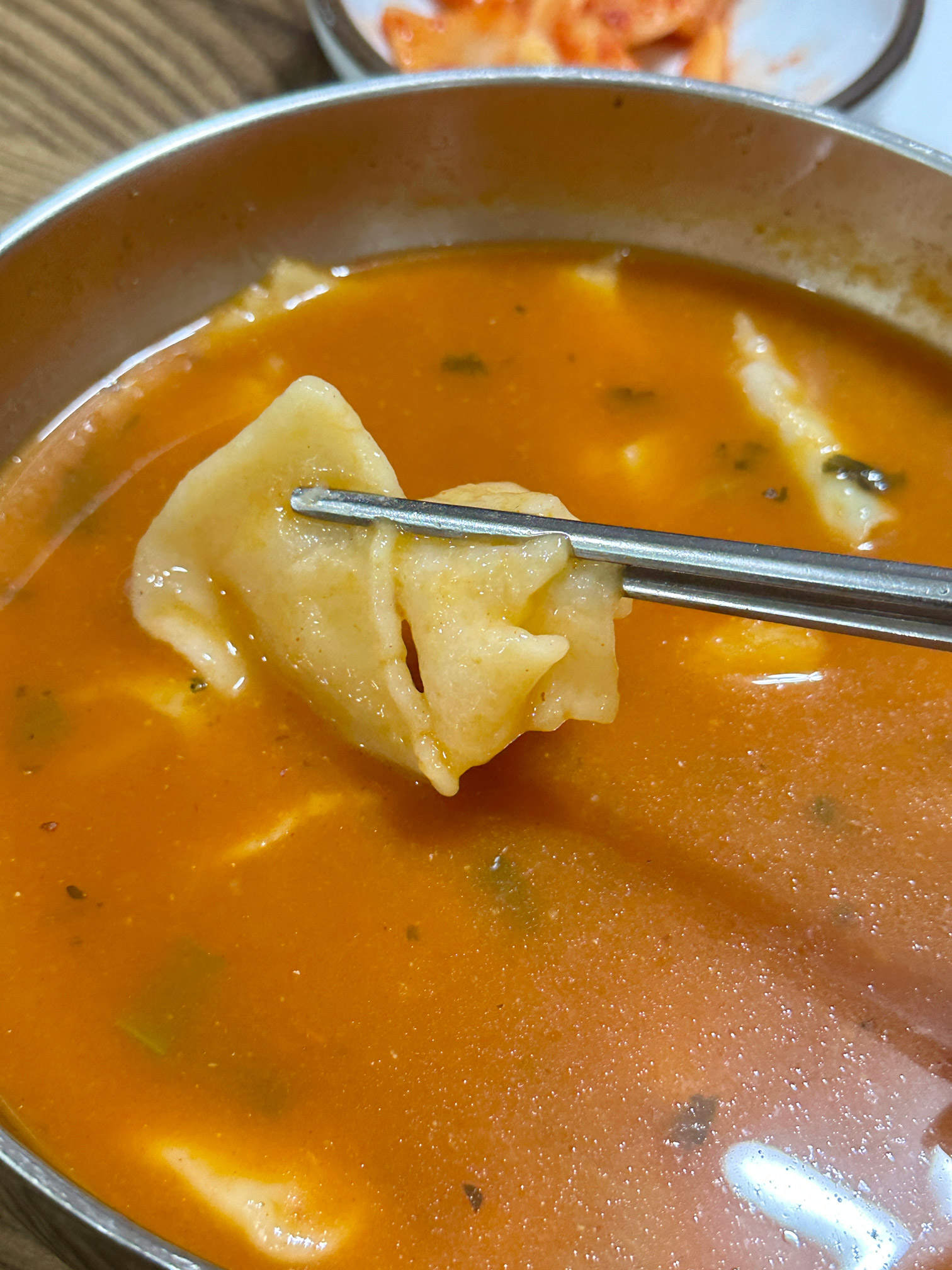 Close-up of spicy sujebi with a steamed mandu lifted on the spoon
