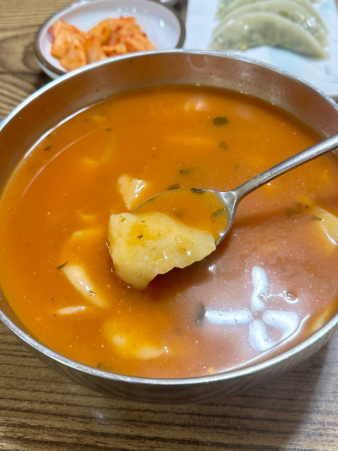 Spoonful of soft hand-torn sujebi noodle lifted from the red broth
