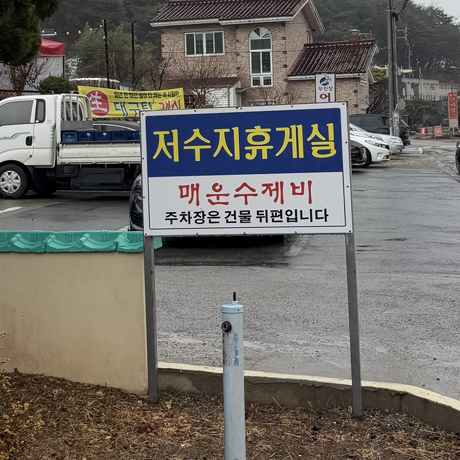 Roadside sign reading Spicy Sujebi and pointing to parking behind the building