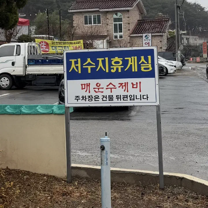 Roadside sign reading Spicy Sujebi and pointing to parking behind the building