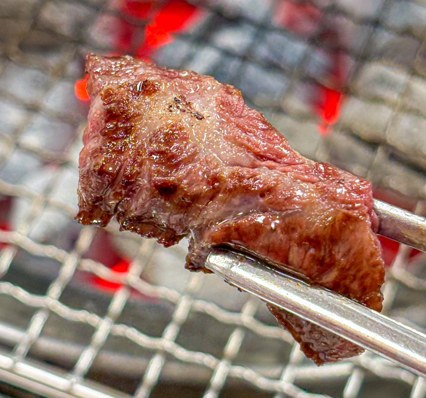 Perfectly grilled Hanwoo galbisal lifted with tongs over the charcoal grill