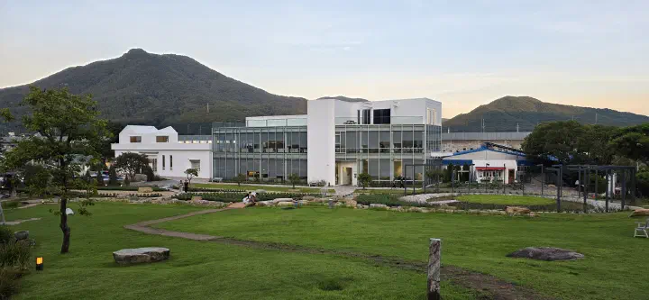 Glass-walled two-story cafe building and lawn garden at Neutinamu-ui Sarang Cafe in Yangsan
