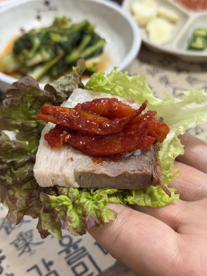 Lettuce wrap holding a slice of suyuk pork topped with spicy pollock salad
