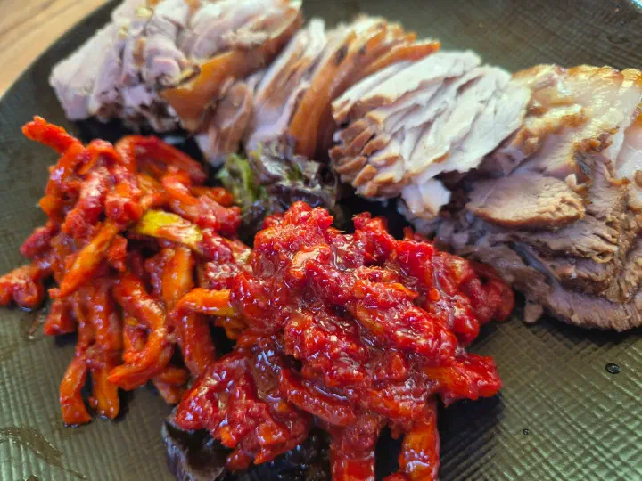 Close-up of tender suyuk pork slices and sweet-spicy myeongtaehoe pollock salad