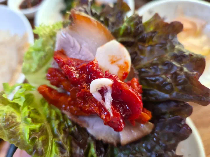 One-bite lettuce wrap of suyuk pork, pollock salad and raw garlic at Yeonggwangjeong Memil Guksu