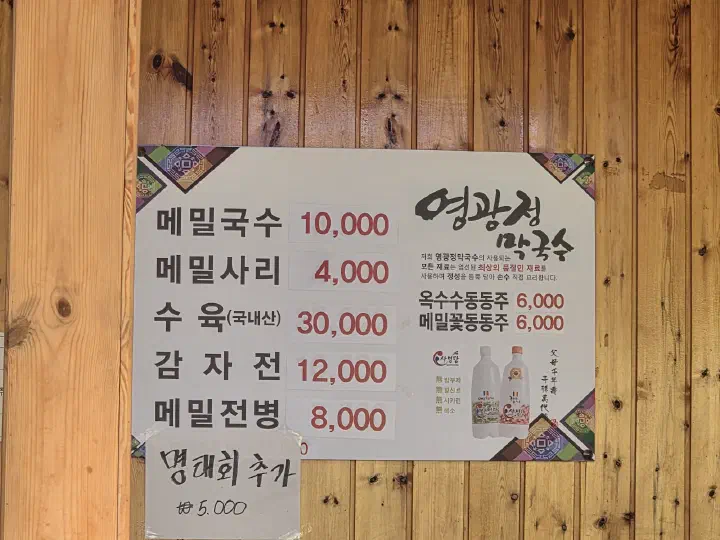 Korean menu board on the wooden wall at Yeonggwangjeong listing memil guksu, suyuk, gamjajeon and jeonbyeong prices
