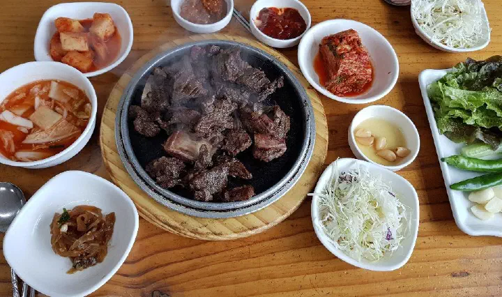 달군 돌판 위 한우 갈비를 위에서 본 모습과 둘러놓인 반찬