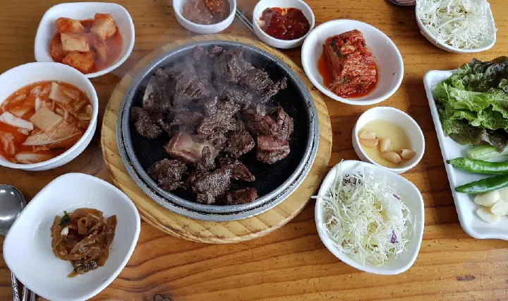 Overhead view of Korean beef ribs on a hot stone plate surrounded by banchan