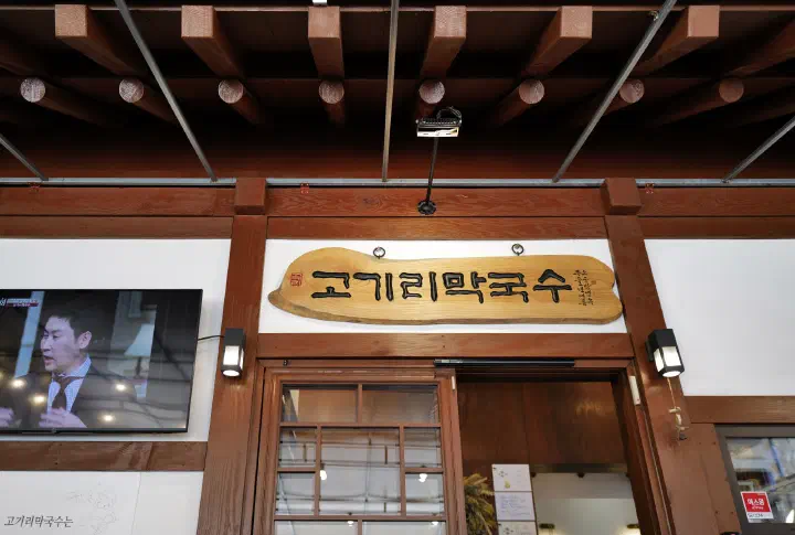 Carved wooden signboard above the entrance of Gogiri Makguksu with a TV screen showing the restaurant&rsquo;s media appearances