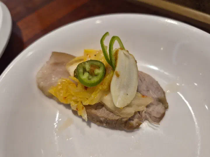 A slice of Gogiri Makguksu suyuk topped with kimchi and green chili as a single bite