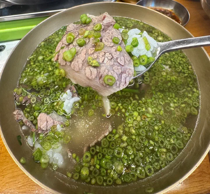A bowl of Neungdong Minari gomtang, clear beef broth piled with finely chopped water dropwort