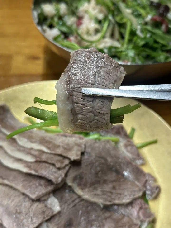 A tender slice of Neungdong Minari boiled beef lifted with chopsticks
